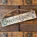 A handmade Christmas sign. Old time writing has been wood-burned onto a piece of reclaimed wood. Reindeer and holly are on either side. 